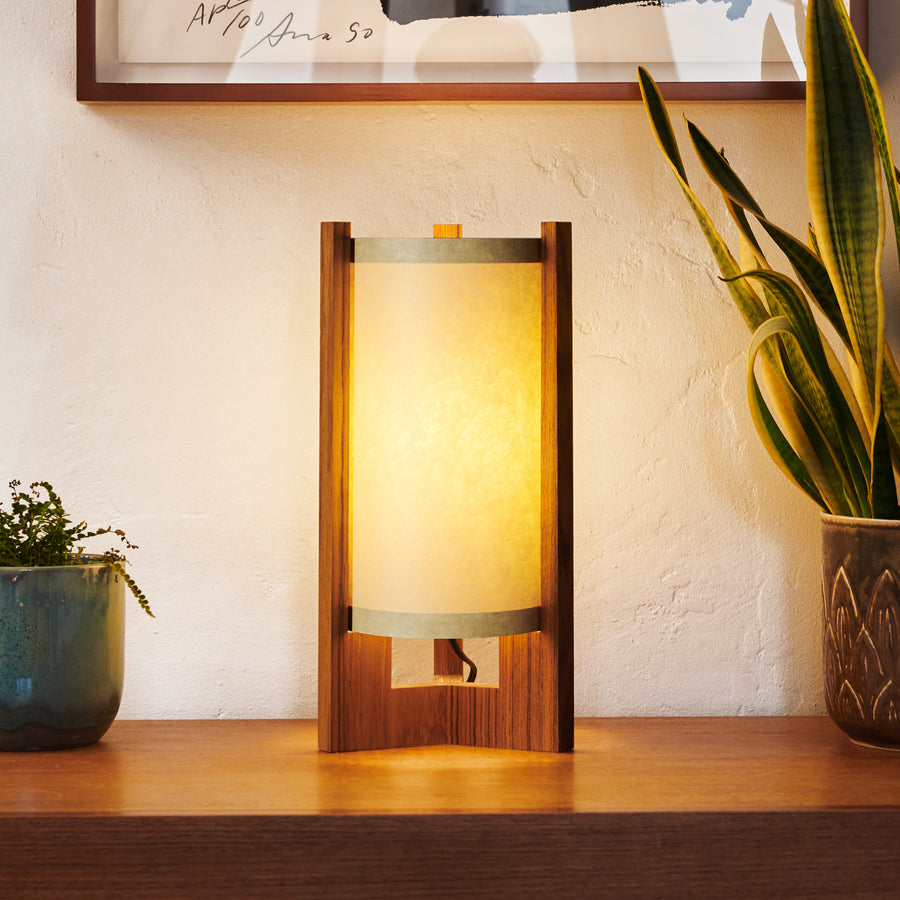 Teak Table Lamp with Sand Lampshade illuminated on dresser next to art and plants