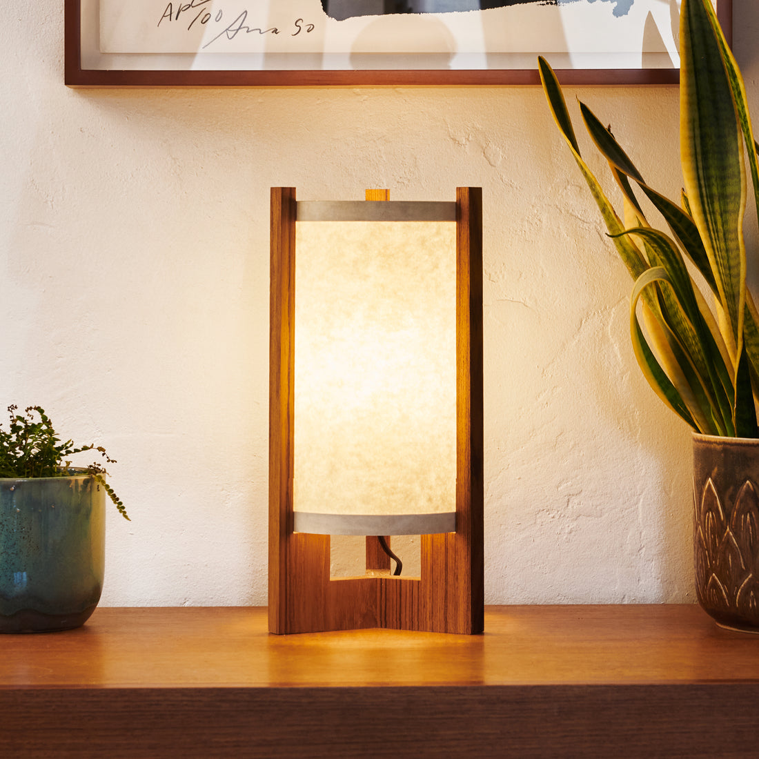 Japanese Mid Century Teak Table Lamp illuminated on counter with plants and art