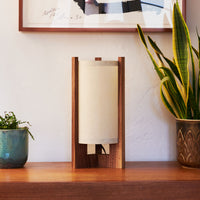 Walnut Table Lamp with Sand Lampshade on dresser next to plants and art